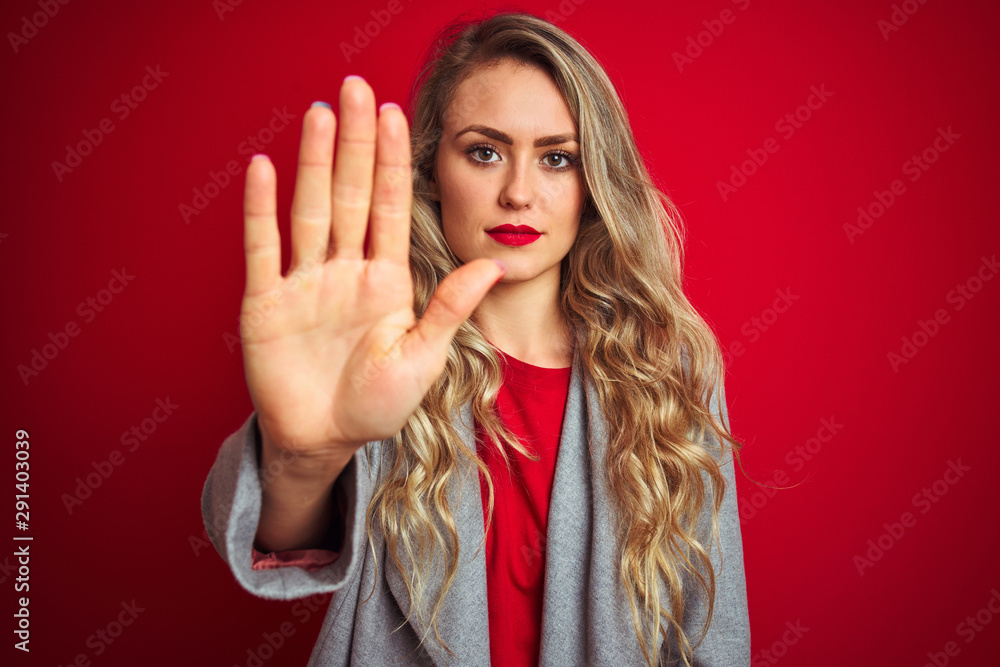 Young beautiful business woman wearing elegant jacket standing over red isolated background doing stop sing with palm of the hand. Warning expression with negative and serious gesture on the face. Young beautiful business woman wearing elegant jacket standing over red isolated background doing stop sing with palm of the hand. Warning expression with negative and serious gesture on the face.