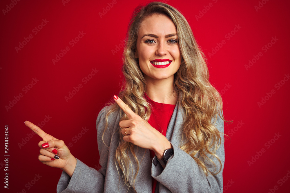Obraz premium Young beautiful business woman wearing elegant jacket standing over red isolated background smiling and looking at the camera pointing with two hands and fingers to the side.