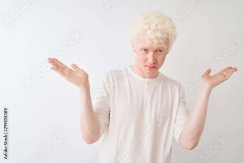Young albino blond man wearing casual t-shirt standing over isolated white background clueless and confused expression with arms and hands raised. Doubt concept.