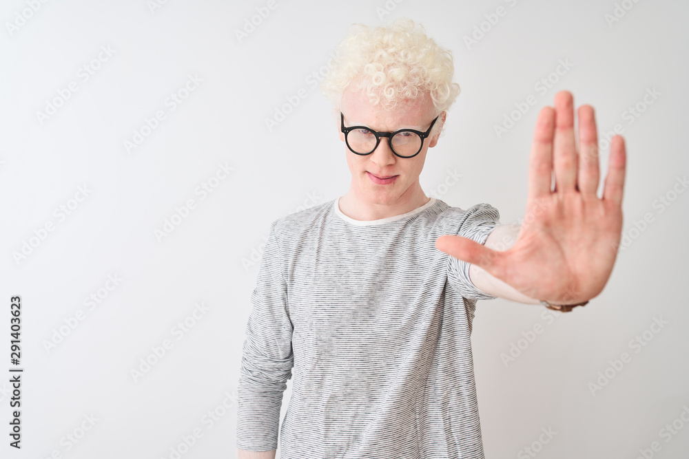Young albino blond man wearing striped t-shirt and glasses over isolated white background doing stop sing with palm of the hand. Warning expression with negative and serious gesture on the face.