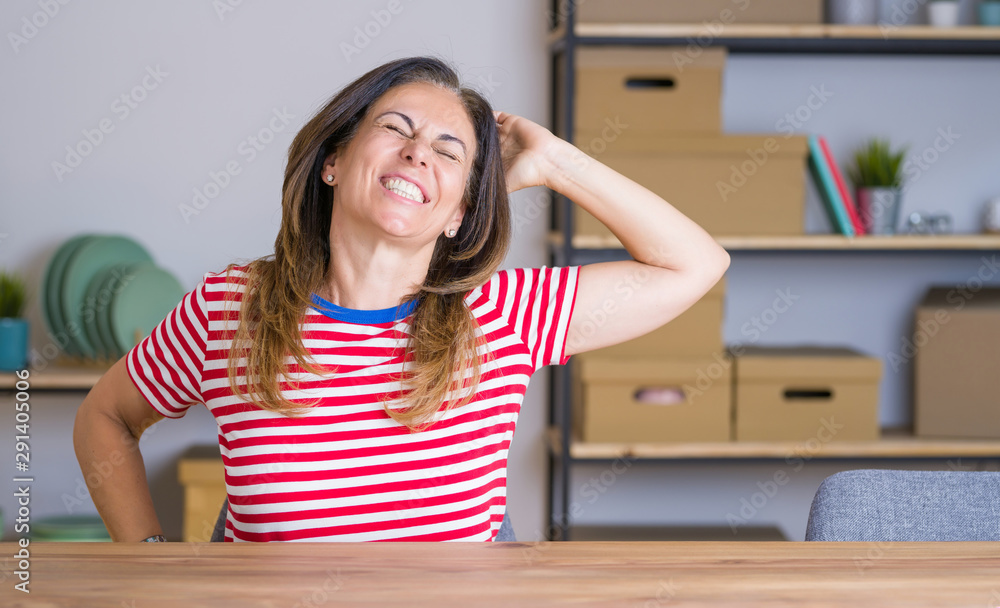Middle age senior woman sitting at the table at home stretching back, tired and relaxed, sleepy and yawning for early morning Middle age senior woman sitting at the table at home stretching back, tired and relaxed, sleepy and yawning for early morning