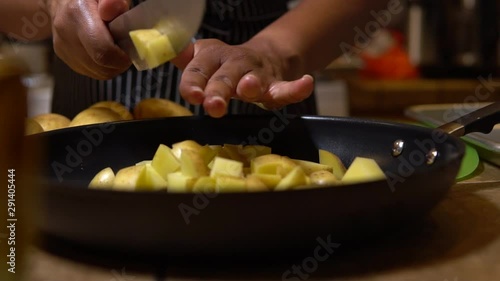 Woman grabs handful of chopped potato and tosses into pan, slow motion photo