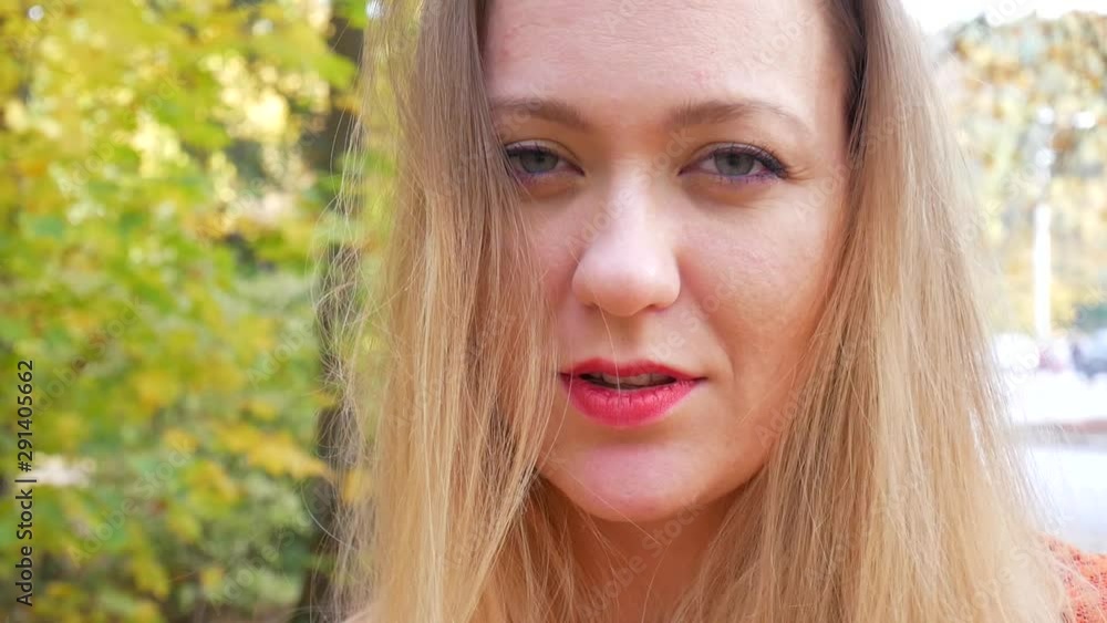 Pretty female winking eye and smiles in forest or park on background of trees with yellow foliage in autumn. Flirting woman concept Pretty female winking eye and smiles in forest or park on background of trees with yellow foliage in autumn. Flirting woman concept