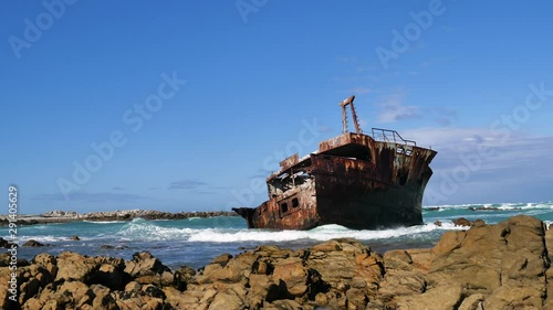 TimeLapse - Rusted old half-shipwreck lying next to rocky coastline of L'Agulhas, waves running in, South Africa