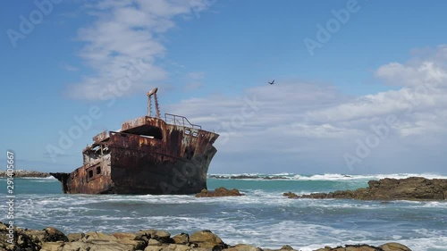 Old weathered shipwreck in shallows with waves running in, rocky coastline of L'Agulhas, South Africa, static shot
