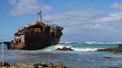 Old weathered shipreck in shallows with waves running in, rocky coastline of L'Agulhas, South Africa, close-up static shot