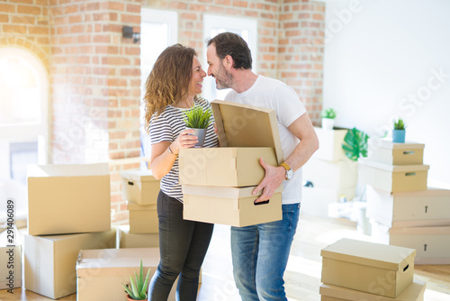 Middle age senior couple moving to a new house, holding cardboard boxing smiling happy in love with apartmant