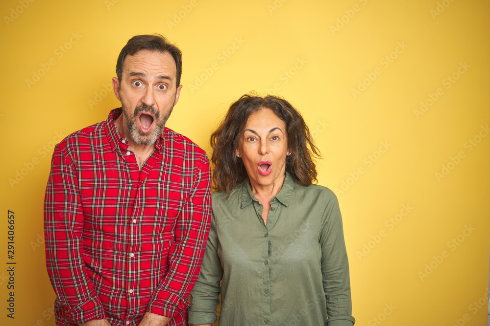 Beautiful middle age couple over isolated yellow background afraid and shocked with surprise expression, fear and excited face. Beautiful middle age couple over isolated yellow background afraid and shocked with surprise expression, fear and excited face.