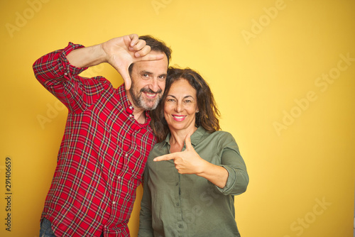 Beautiful middle age couple over isolated yellow background smiling making frame with hands and fingers with happy face. Creativity and photography concept.