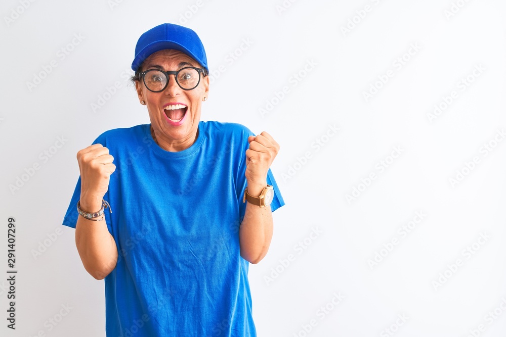 Senior deliverywoman wearing cap and glasses standing over isolated white background celebrating surprised and amazed for success with arms raised and open eyes. Winner concept.