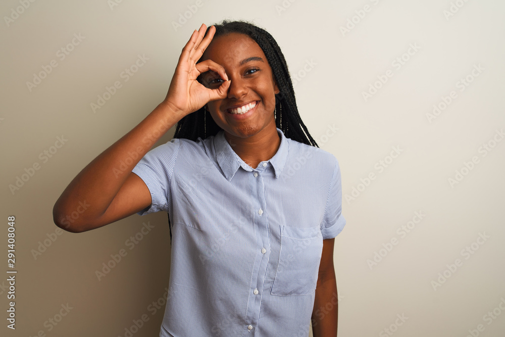 Young african american woman wearing striped shirt standing over isolated white background doing ok gesture with hand smiling, eye looking through fingers with happy face. Young african american woman wearing striped shirt standing over isolated white background doing ok gesture with hand smiling, eye looking through fingers with happy face.