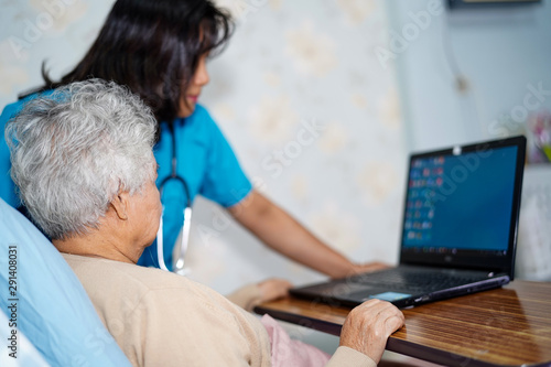 Doctor teach and suggest Asian senior or elderly old lady woman patient to using notebook computer while sitting on bed in nursing hospital ward : healthy strong medical concept..
