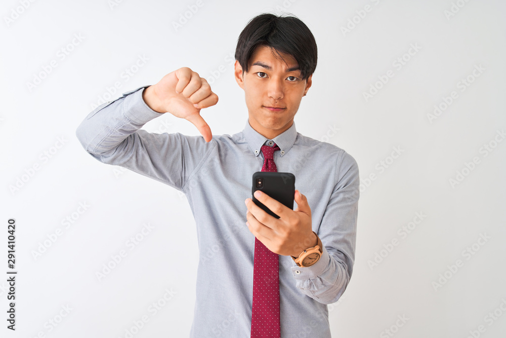 Chinese businessman wearing tie using smartphone standing over isolated white background with angry face, negative sign showing dislike with thumbs down, rejection concept Chinese businessman wearing tie using smartphone standing over isolated white background with angry face, negative sign showing dislike with thumbs down, rejection concept