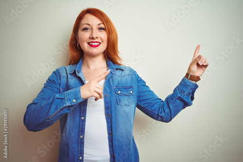 Young beautiful redhead woman wearing denim shirt standing over white isolated background smiling and looking at the camera pointing with two hands and fingers to the side.