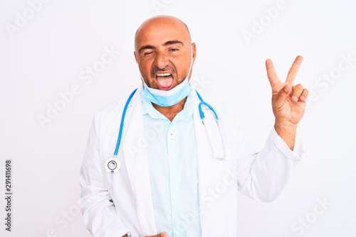 Middle age doctor man wearing stethoscope and mask over isolated white background smiling with happy face winking at the camera doing victory sign. Number two.