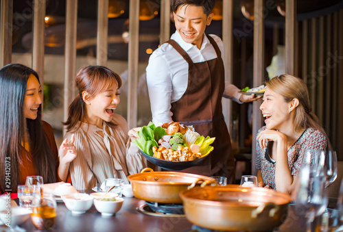 waiter  bring  vegetables for hot pot  and serving group of friends in restaurant