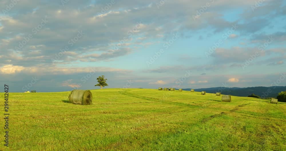 Agricultural machine riding on the horizon of a hill with an abandoned tree during the day with a view of a stack of hay and a view of moving clouds and the nature panoramic view of the countryside. Agricultural machine riding on the horizon of a hill with an abandoned tree during the day with a view of a stack of hay and a view of moving clouds and the nature panoramic view of the countryside.