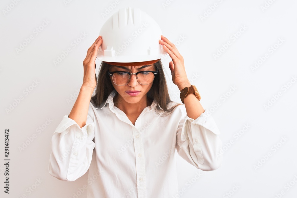 Young beautiful architect woman wearing helmet and glasses over isolated white background suffering from headache desperate and stressed because pain and migraine. Hands on head. Young beautiful architect woman wearing helmet and glasses over isolated white background suffering from headache desperate and stressed because pain and migraine. Hands on head.