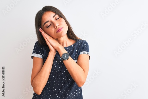 Young beautiful woman wearing blue casual t-shirt standing over isolated white background sleeping tired dreaming and posing with hands together while smiling with closed eyes.