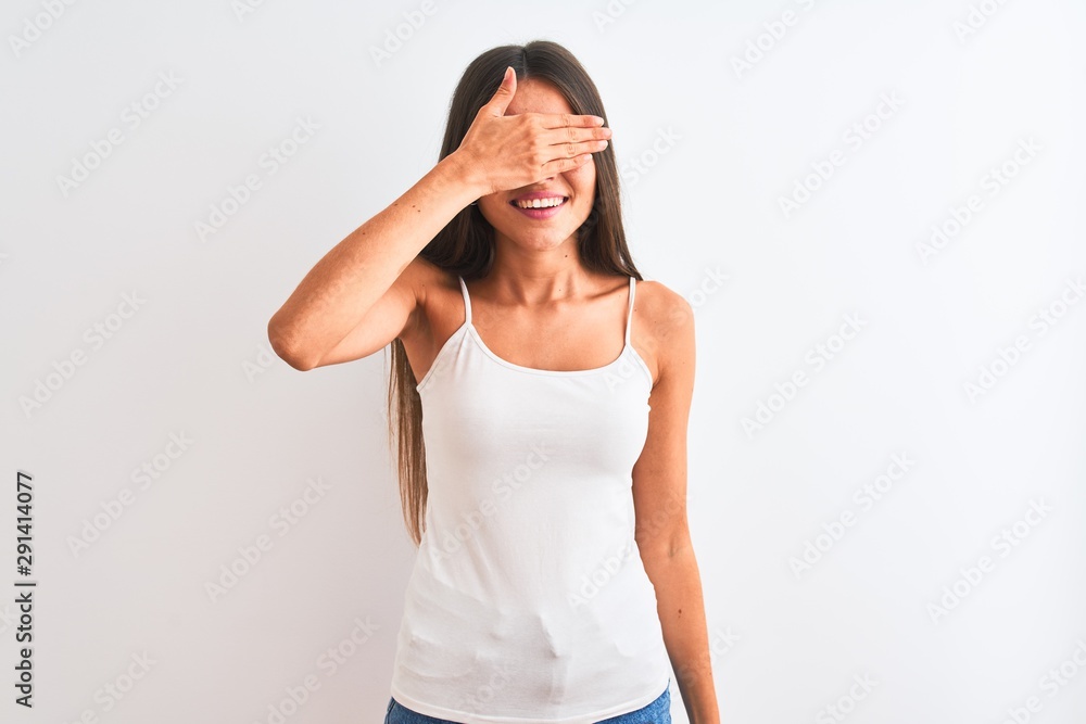 Young beautiful woman wearing casual t-shirt standing over isolated white background smiling and laughing with hand on face covering eyes for surprise. Blind concept. Young beautiful woman wearing casual t-shirt standing over isolated white background smiling and laughing with hand on face covering eyes for surprise. Blind concept.