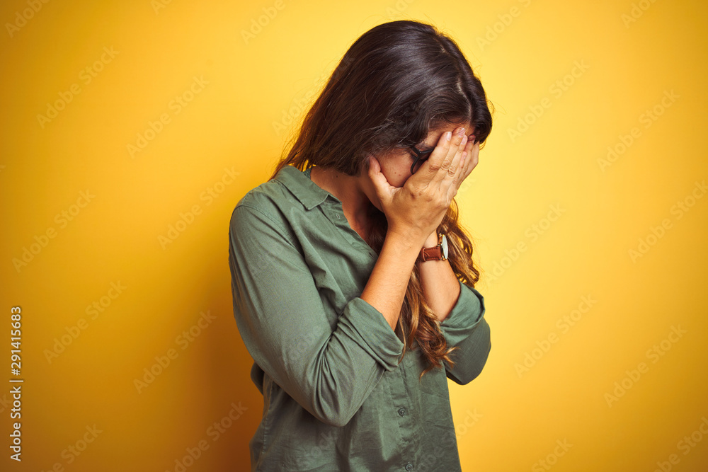 Young beautiful woman wearing green shirt and glasses over yelllow isolated background with sad expression covering face with hands while crying. Depression concept. Young beautiful woman wearing green shirt and glasses over yelllow isolated background with sad expression covering face with hands while crying. Depression concept.