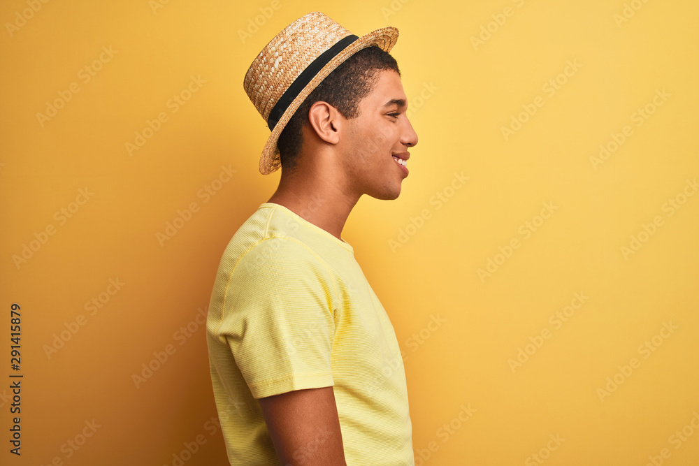 Young handsome arab man wearing t-shirt and summer hat over isolated yelllow background looking to side, relax profile pose with natural face with confident smile. Young handsome arab man wearing t-shirt and summer hat over isolated yelllow background looking to side, relax profile pose with natural face with confident smile.