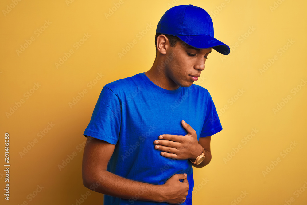 Young handsome arab delivery man standing over isolated yellow background with hand on stomach because nausea, painful disease feeling unwell. Ache concept. Young handsome arab delivery man standing over isolated yellow background with hand on stomach because nausea, painful disease feeling unwell. Ache concept.