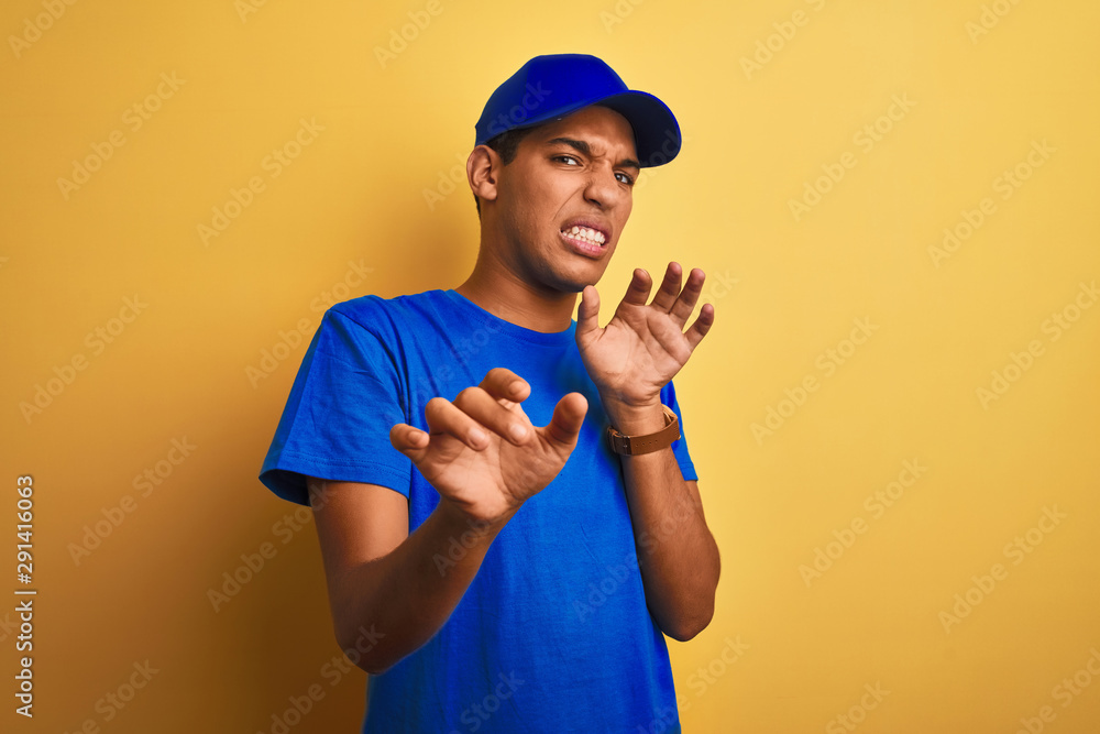 Young handsome arab delivery man standing over isolated yellow background disgusted expression, displeased and fearful doing disgust face because aversion reaction. With hands raised Young handsome arab delivery man standing over isolated yellow background disgusted expression, displeased and fearful doing disgust face because aversion reaction. With hands raised