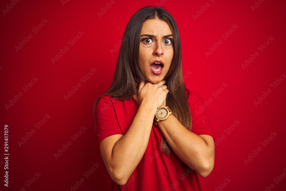 Young beautiful woman wearing t-shirt standing over isolated red background shouting and suffocate because painful strangle. Health problem. Asphyxiate and suicide concept. Young beautiful woman wearing t-shirt standing over isolated red background shouting and suffocate because painful strangle. Health problem. Asphyxiate and suicide concept.