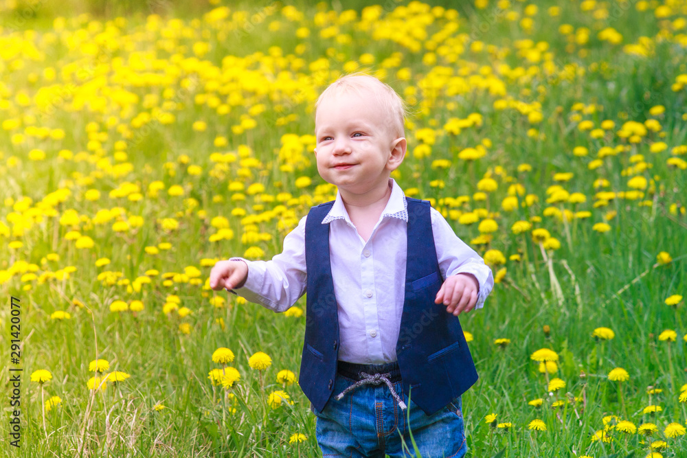Toddler boy in a trendy stylish suit on a glade of blooming yellow dandelion flowers. series Emotions and laughter of a little boy. spring and bloom. Toddler boy in a trendy stylish suit on a glade of blooming yellow dandelion flowers. series Emotions and laughter of a little boy. spring and bloom.