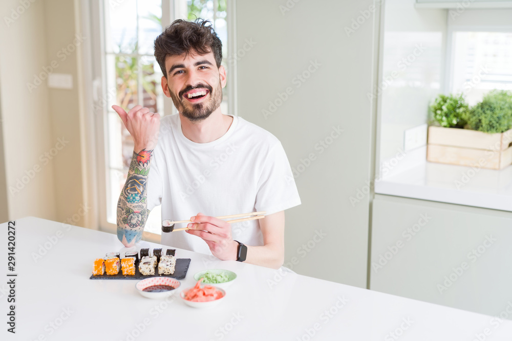 Young man eating asian sushi from home delivery pointing and showing with thumb up to the side with happy face smiling Young man eating asian sushi from home delivery pointing and showing with thumb up to the side with happy face smiling
