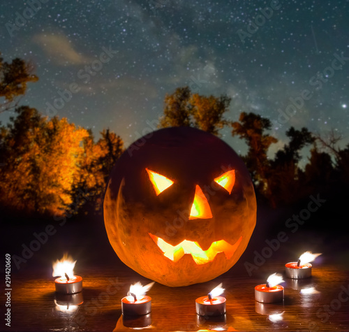 halloween night scene, jack o lantern pumpkin arond candle on the night forest glade under starry sky photo