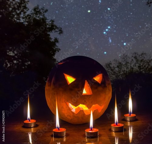 halloween night scene, jack o lantern pumpkin arond candle on the night forest glade under starry sky photo