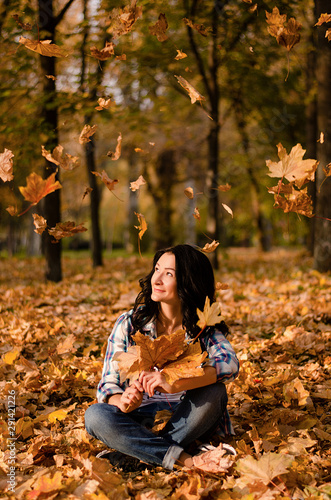 Beautiful woman sitting on the ground on yellow leaves in park. Leisure time on warm autumn day