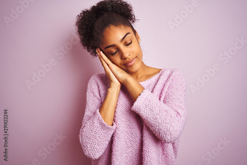 Young african american woman wearing winter sweater standing over isolated pink background sleeping tired dreaming and posing with hands together while smiling with closed eyes.