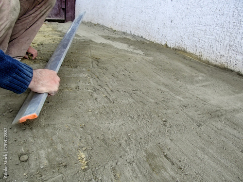 A man smooths the surface of a cement-sand mixture with an aluminium plasterers feather edge tool. Preparation of the site for laying paving slabs, work on the improvement of the yard or pavement