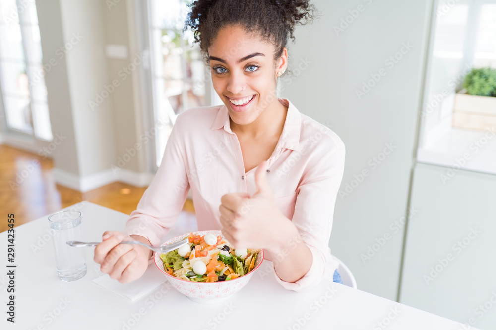 Young african american woman eating healthy pasta salad happy with big smile doing ok sign, thumb up with fingers, excellent sign