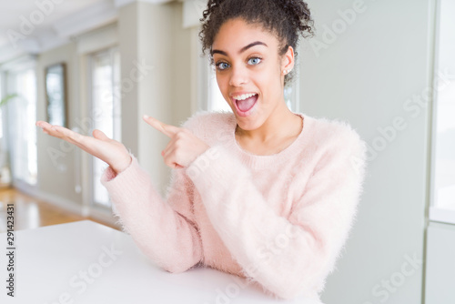 Beautiful young african american woman with afro hair amazed and smiling to the camera while presenting with hand and pointing with finger.