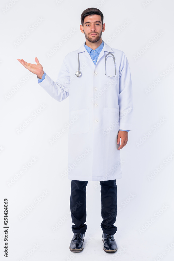 Full body shot of young bearded Persian man doctor showing something Full body shot of young bearded Persian man doctor showing something