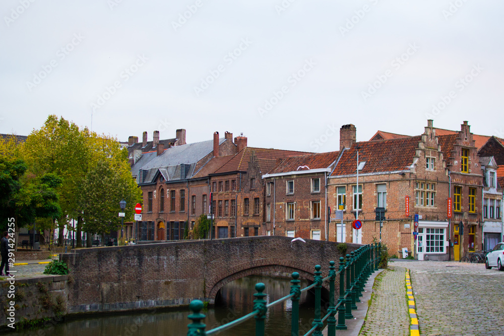 Ghent, Belgium; 10/29/2018: Typical belgian street in Patershol with green railings, Lys river and a brick bridge at the background, with houses and trees