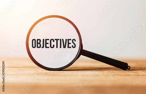 Magnifying glass with text Objectives on wooden table. photo