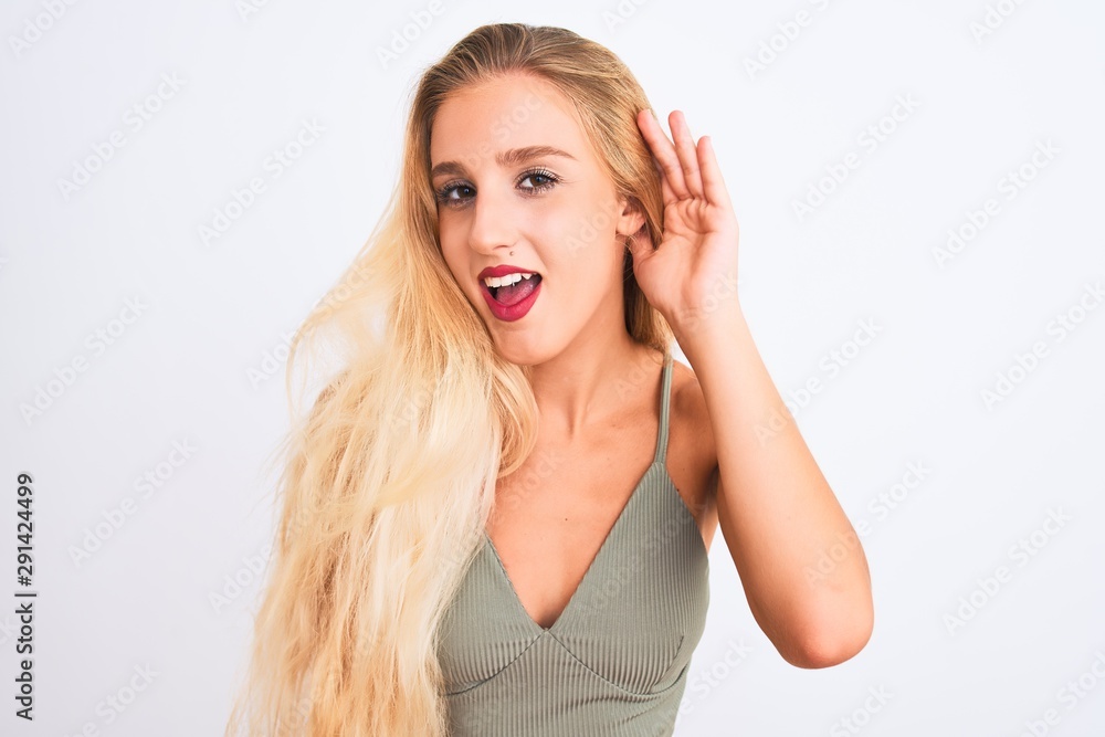 Young beautiful woman wearing casual green t-shirt standing over isolated white background smiling with hand over ear listening an hearing to rumor or gossip. Deafness concept. Young beautiful woman wearing casual green t-shirt standing over isolated white background smiling with hand over ear listening an hearing to rumor or gossip. Deafness concept.