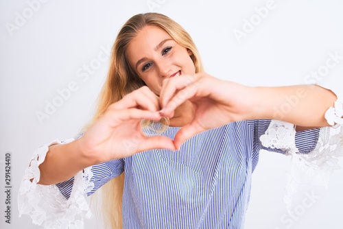 Young beautiful woman wearing elegant blue t-shirt standing over isolated white background smiling in love showing heart symbol and shape with hands. Romantic concept.