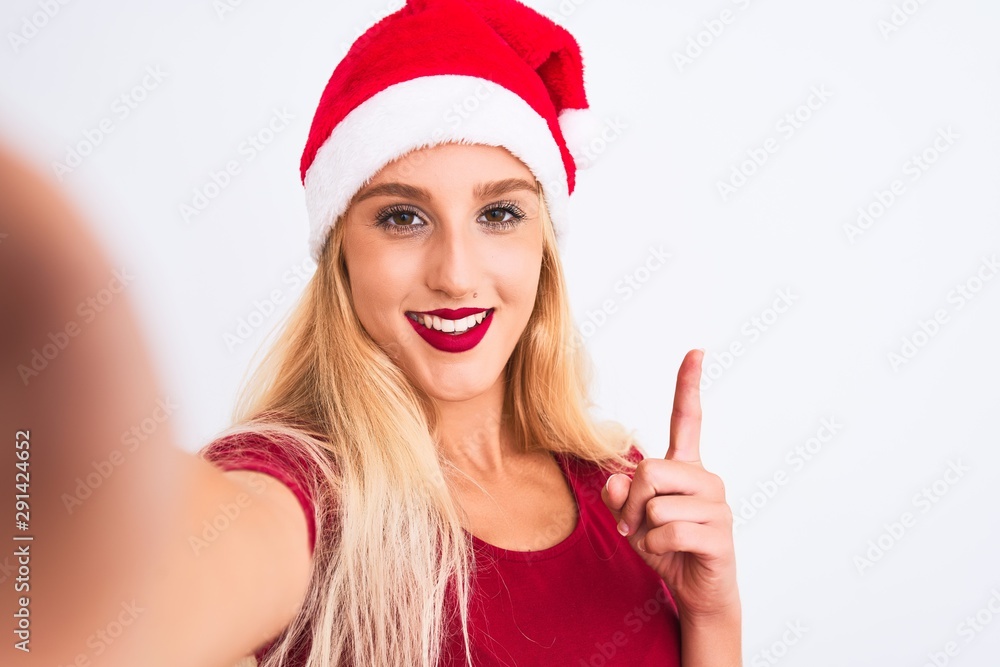 Woman wearing Christmas Santa hat make selfie by camera over isolated white background surprised with an idea or question pointing finger with happy face, number one Woman wearing Christmas Santa hat make selfie by camera over isolated white background surprised with an idea or question pointing finger with happy face, number one