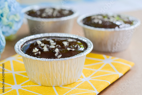 Dark chocolate cake with chocolate chips topping in round foil cup on yellow tablecloth and wooden table. Copy space for your text. Selective focus.