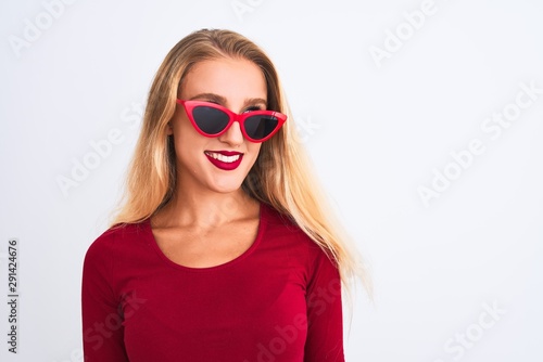 Young beautiful woman wearing red t-shirt and sunglasses over isolated white background looking away to side with smile on face, natural expression. Laughing confident.