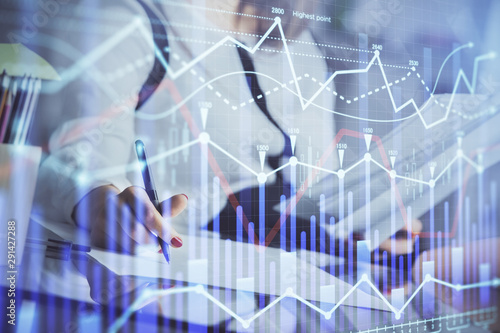 A woman hands writing information about stock market in notepad. Forex chart holograms in front. Concept of research.