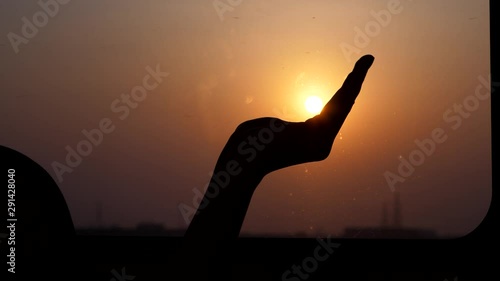 Woman hold setting sun on hand, then grab it into fist, silhouetted shot. Arm of female passenger against train window, blurred background, slow motion shot photo