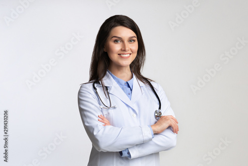 Smiling Female Doctor Standing Crossing Hands Over White Background photo