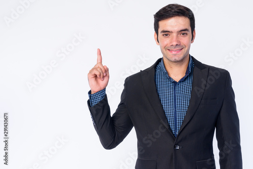 Portrait of happy young handsome Persian businessman in suit pointing up